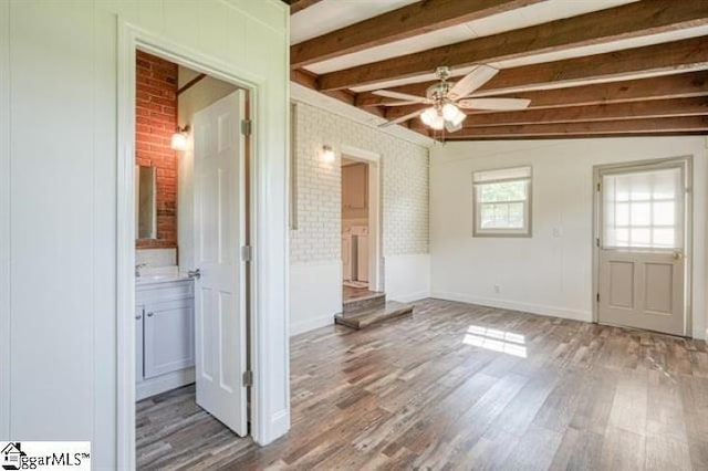 spare room featuring ceiling fan, hardwood / wood-style flooring, beamed ceiling, and brick wall