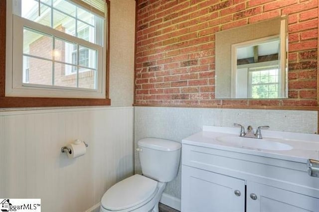 bathroom featuring brick wall, vanity, toilet, and a wealth of natural light