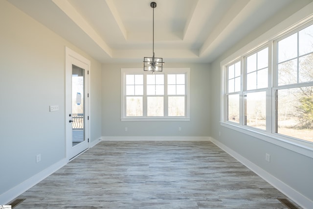 unfurnished dining area with light hardwood / wood-style flooring, a notable chandelier, a tray ceiling, and plenty of natural light