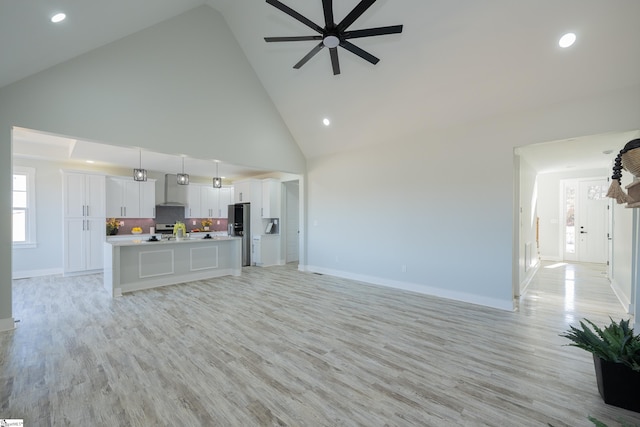 unfurnished living room with light hardwood / wood-style flooring, high vaulted ceiling, and ceiling fan