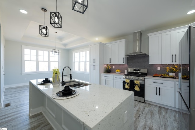 kitchen featuring wall chimney range hood, stainless steel gas range, white cabinetry, a tray ceiling, and decorative light fixtures