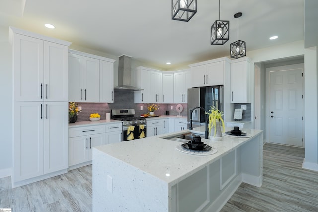 kitchen with appliances with stainless steel finishes, pendant lighting, white cabinetry, light stone countertops, and wall chimney range hood