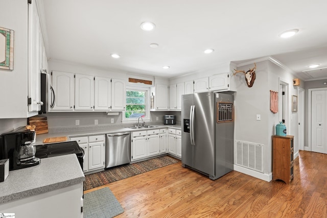 kitchen featuring sink, appliances with stainless steel finishes, wood-type flooring, ornamental molding, and white cabinets