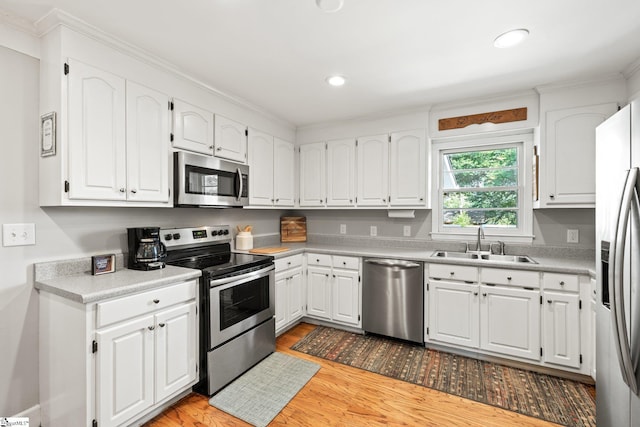 kitchen featuring sink, light hardwood / wood-style flooring, ornamental molding, stainless steel appliances, and white cabinets