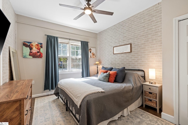 bedroom with ceiling fan, brick wall, and light wood-type flooring