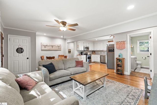 living room with crown molding, ceiling fan, and light wood-type flooring