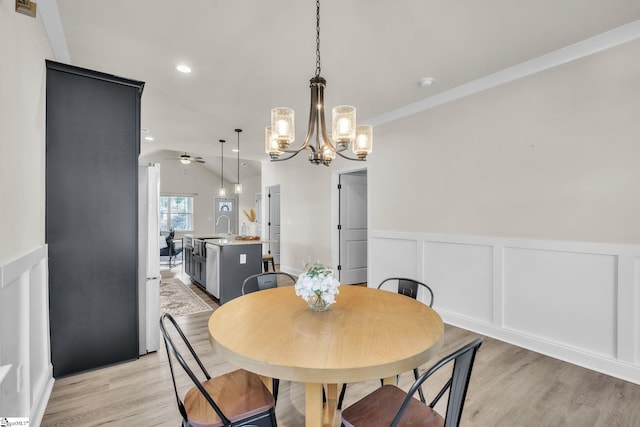 dining area featuring lofted ceiling, sink, crown molding, light wood-type flooring, and ceiling fan with notable chandelier