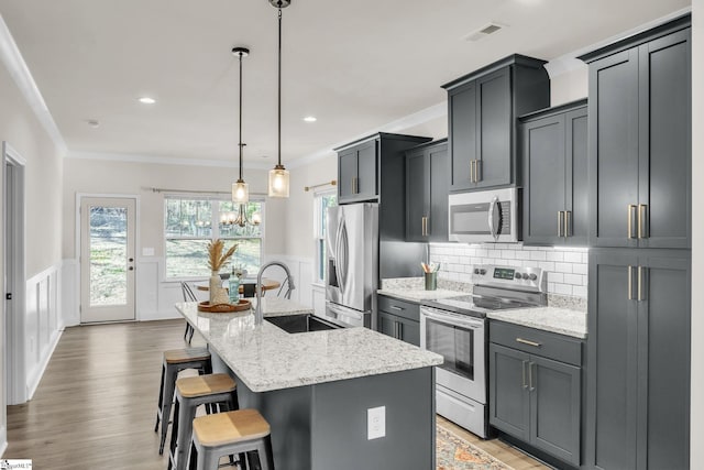 kitchen with a breakfast bar area, hanging light fixtures, stainless steel appliances, light stone countertops, and a center island with sink