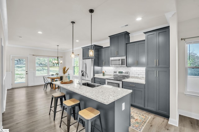 kitchen with sink, decorative light fixtures, appliances with stainless steel finishes, an island with sink, and light stone countertops