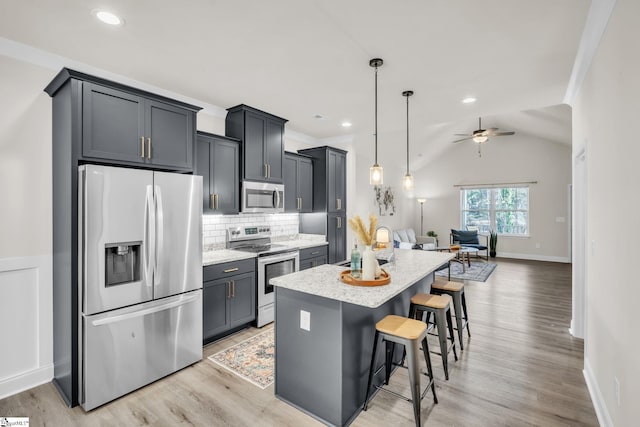 kitchen featuring a breakfast bar area, tasteful backsplash, hanging light fixtures, appliances with stainless steel finishes, and an island with sink