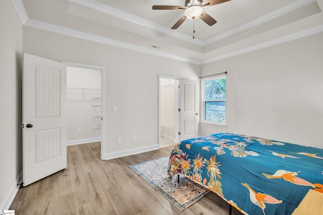 bedroom featuring crown molding, light hardwood / wood-style floors, a raised ceiling, a spacious closet, and a closet