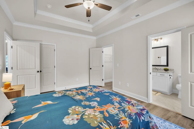 bedroom with crown molding, ensuite bath, light hardwood / wood-style floors, a raised ceiling, and a closet