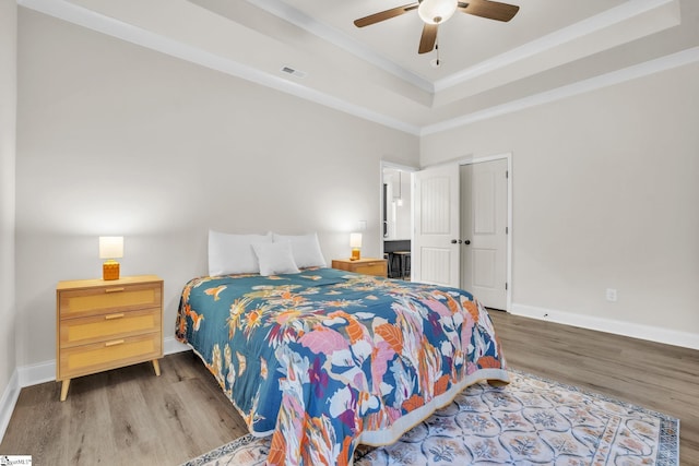 bedroom with ceiling fan, hardwood / wood-style floors, a tray ceiling, ornamental molding, and a closet