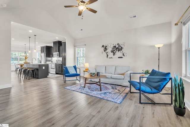 living room featuring vaulted ceiling, sink, ceiling fan, and light wood-type flooring