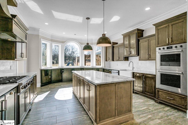 kitchen with premium range hood, sink, hanging light fixtures, appliances with stainless steel finishes, and a kitchen island