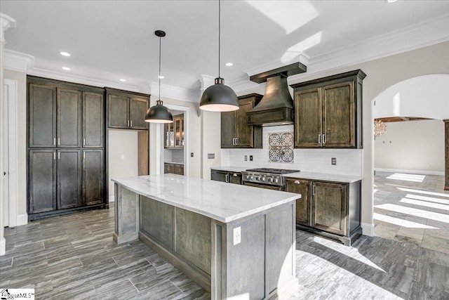 kitchen with hanging light fixtures, a center island, dark brown cabinetry, light stone countertops, and custom range hood