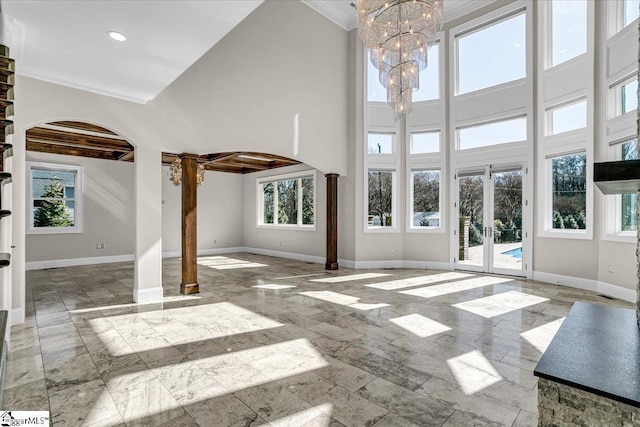 unfurnished living room featuring a notable chandelier, ornamental molding, decorative columns, and a high ceiling