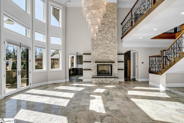 unfurnished living room with a notable chandelier, a stone fireplace, ornamental molding, and a high ceiling