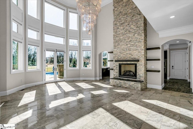 unfurnished living room featuring a towering ceiling, ornamental molding, a stone fireplace, and a chandelier