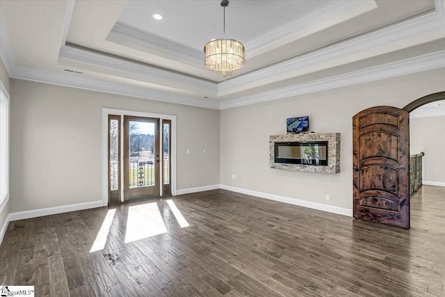 unfurnished living room featuring ornamental molding, a chandelier, dark hardwood / wood-style flooring, and a tray ceiling