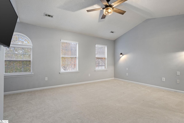 spare room featuring ceiling fan, vaulted ceiling, light carpet, and a textured ceiling