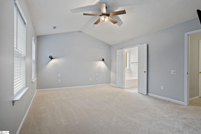 unfurnished bedroom featuring lofted ceiling, connected bathroom, light colored carpet, a textured ceiling, and ceiling fan