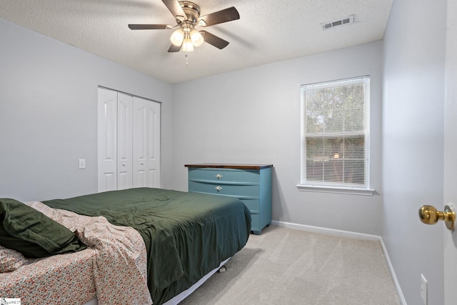 bedroom featuring ceiling fan, light colored carpet, a closet, and a textured ceiling