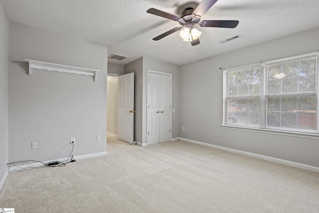 unfurnished bedroom with ceiling fan, light carpet, and a textured ceiling