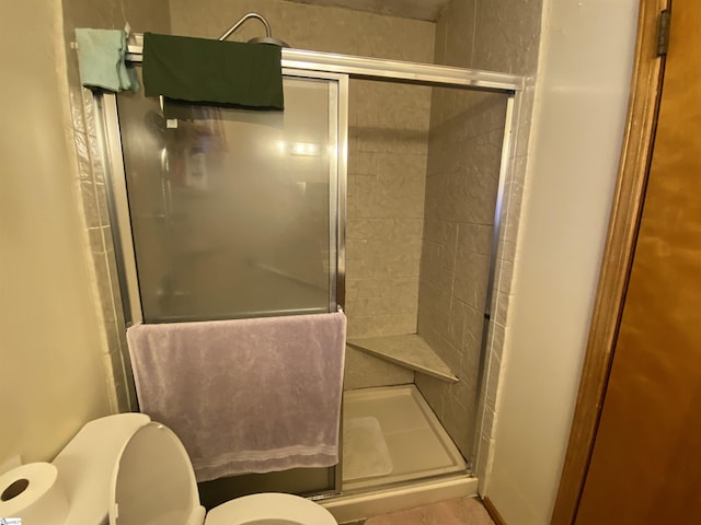 bathroom featuring toilet and a shower with shower door