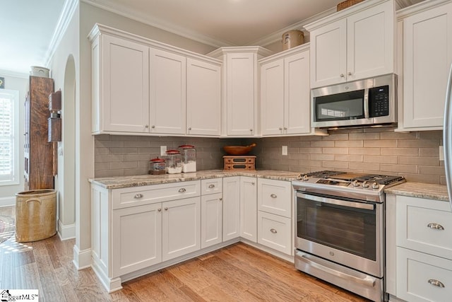 kitchen with white cabinets, ornamental molding, light hardwood / wood-style floors, stainless steel appliances, and light stone countertops