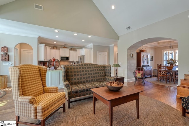 living room with an inviting chandelier, high vaulted ceiling, ornamental molding, and light hardwood / wood-style floors