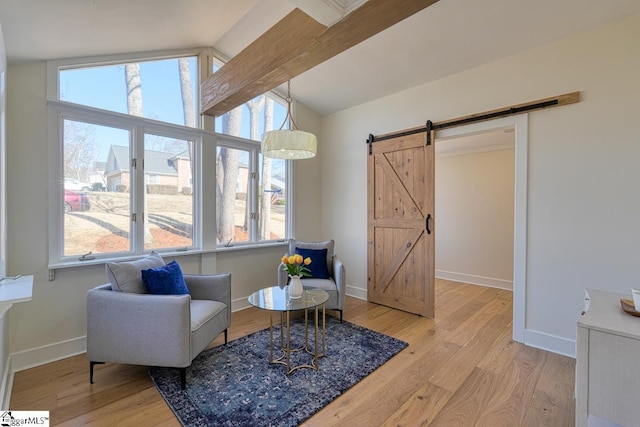 sitting room with a barn door, lofted ceiling with beams, and light hardwood / wood-style flooring