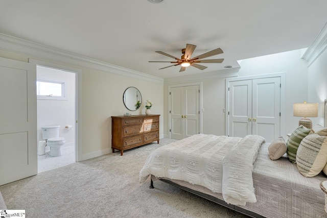 bedroom featuring ceiling fan, ensuite bathroom, ornamental molding, two closets, and light colored carpet