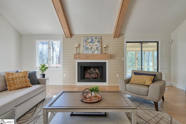 living room with a fireplace, beam ceiling, plenty of natural light, and light wood-type flooring