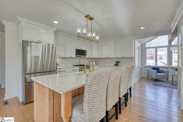 kitchen featuring white cabinetry, light stone counters, hanging light fixtures, an island with sink, and stainless steel appliances