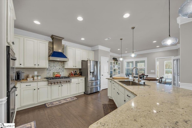 kitchen featuring wall chimney exhaust hood, sink, decorative light fixtures, appliances with stainless steel finishes, and light stone countertops