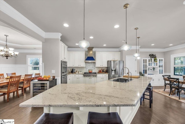 kitchen featuring sink, appliances with stainless steel finishes, hanging light fixtures, a kitchen breakfast bar, and wall chimney exhaust hood