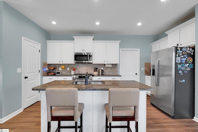 kitchen with stainless steel appliances, an island with sink, sink, and white cabinets