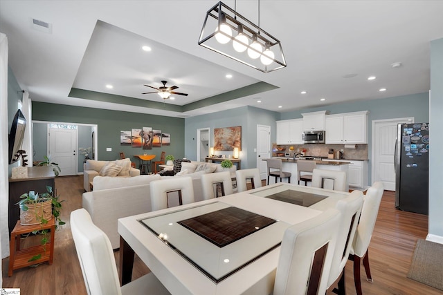 dining space featuring a tray ceiling, wood-type flooring, and ceiling fan