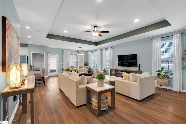 living room with ceiling fan with notable chandelier, hardwood / wood-style floors, and a tray ceiling