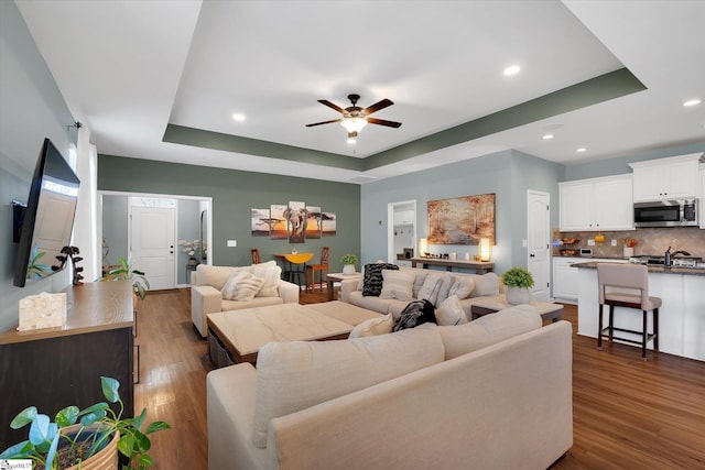 living room with dark hardwood / wood-style floors, ceiling fan, and a tray ceiling