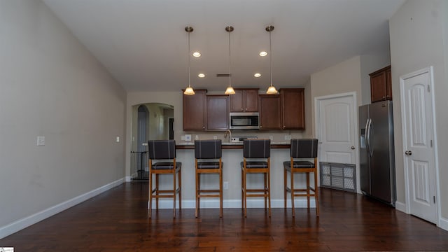 kitchen with dark hardwood / wood-style flooring, hanging light fixtures, an island with sink, and appliances with stainless steel finishes