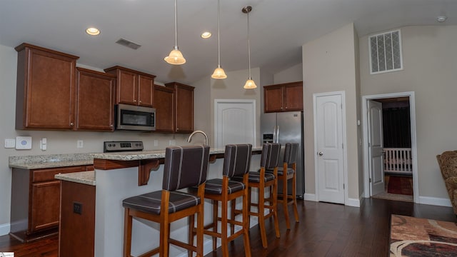 kitchen with appliances with stainless steel finishes, decorative light fixtures, an island with sink, a kitchen breakfast bar, and light stone counters