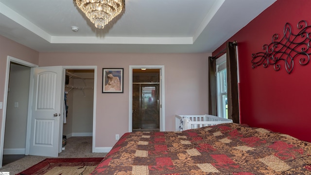 carpeted bedroom with an inviting chandelier, a tray ceiling, a walk in closet, and ensuite bath