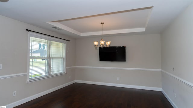 spare room with dark hardwood / wood-style floors, a tray ceiling, and an inviting chandelier