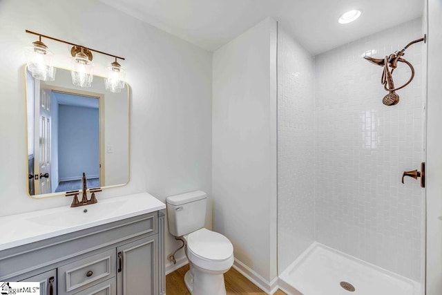 bathroom with a tile shower, vanity, wood-type flooring, and toilet