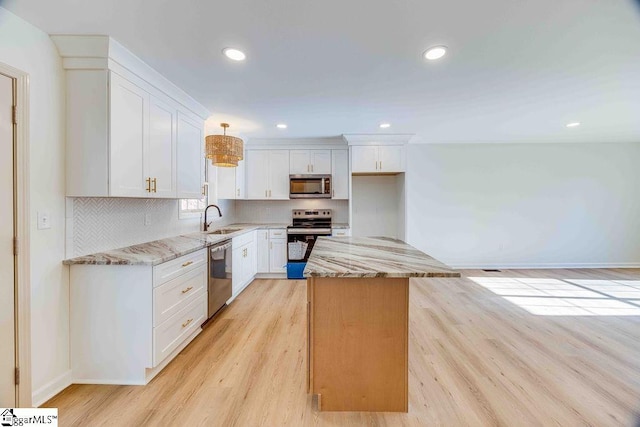 kitchen with sink, white cabinetry, stainless steel appliances, a center island, and light stone counters