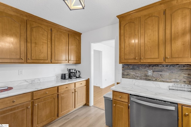 kitchen with tasteful backsplash, light hardwood / wood-style flooring, a textured ceiling, stainless steel dishwasher, and light stone countertops