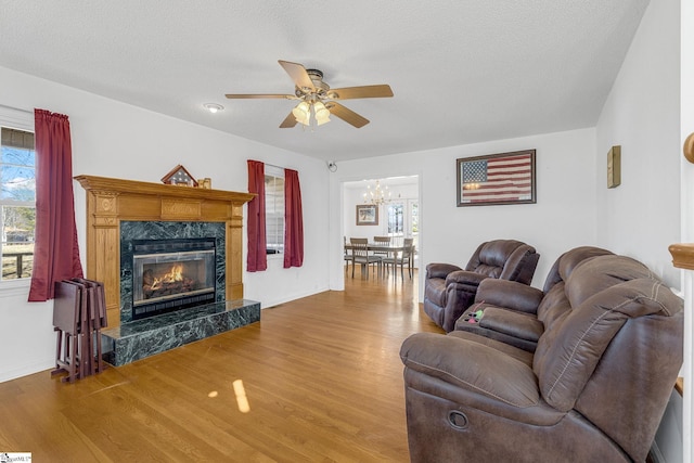 living room with hardwood / wood-style flooring, a wealth of natural light, a premium fireplace, and ceiling fan with notable chandelier