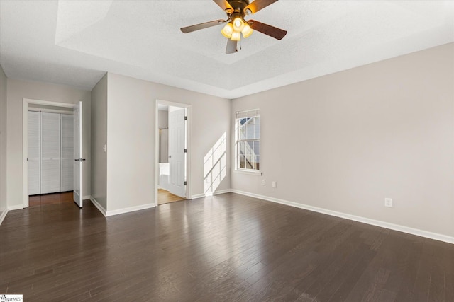 empty room featuring a raised ceiling, ceiling fan, dark hardwood / wood-style floors, and a textured ceiling